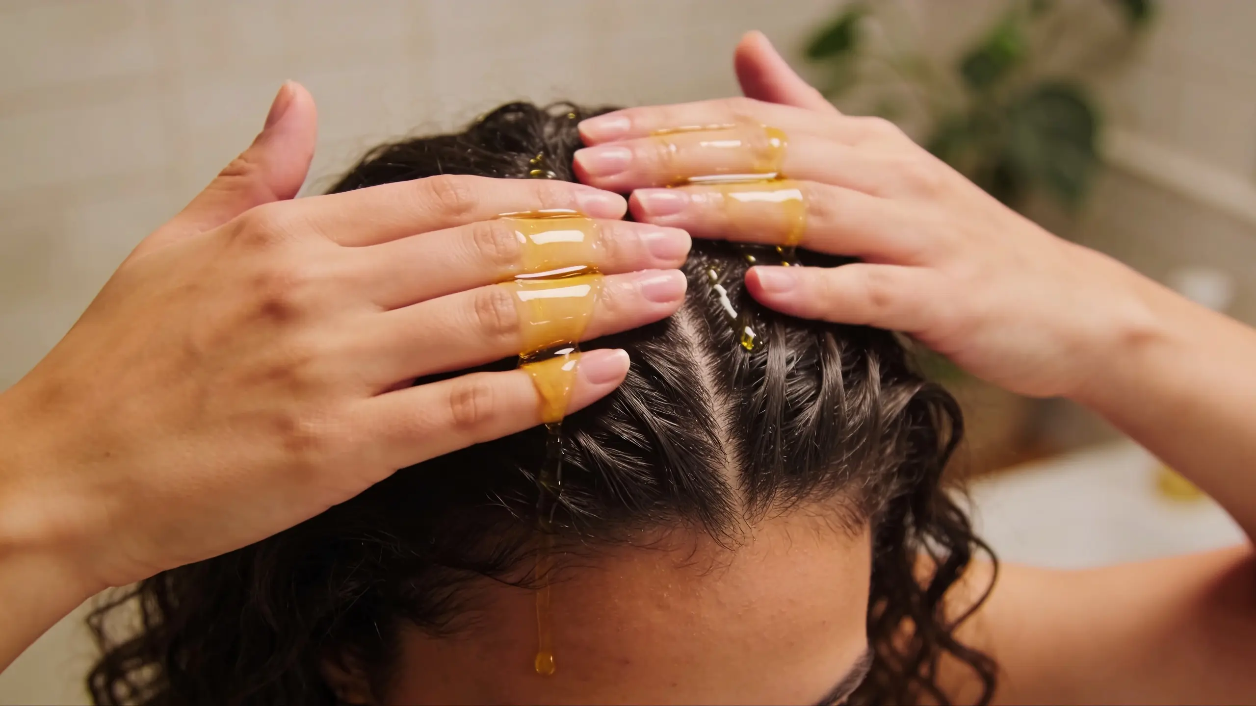 Woman massaging oil into her scalp with fingertips, warm bathroom lighting